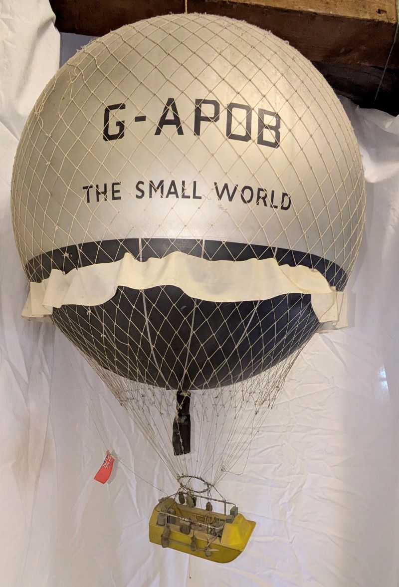 Picture of a 3-d model of a traditional netted gas balloon with a silver coloured top third and black lower third. Suspended beneath is a small boat instead of a basket